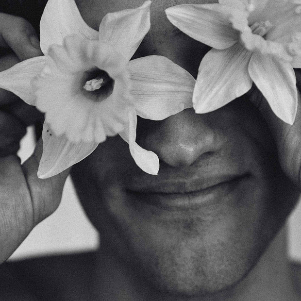 Photo mood pour le parfum naturel La Terre : visage masculin dont les yeux sont cachés par des jonquilles, en noir et blanc